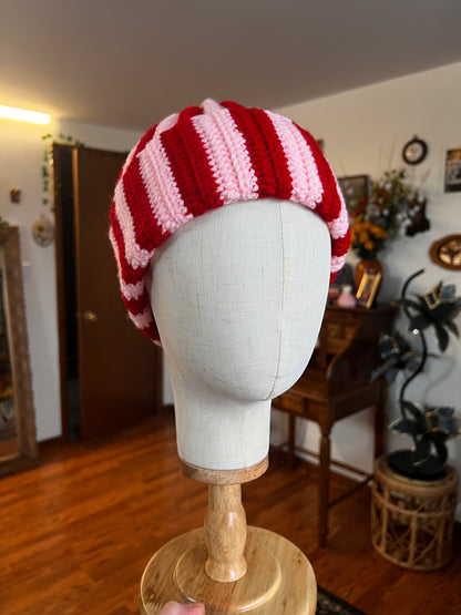Red and pink striped beanie on a mannequin head with a blurred indoor background