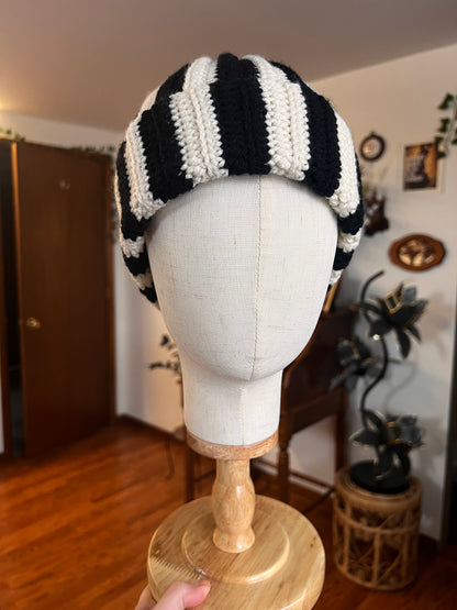 Mannequin head with black and white striped hat on a wooden stand.
