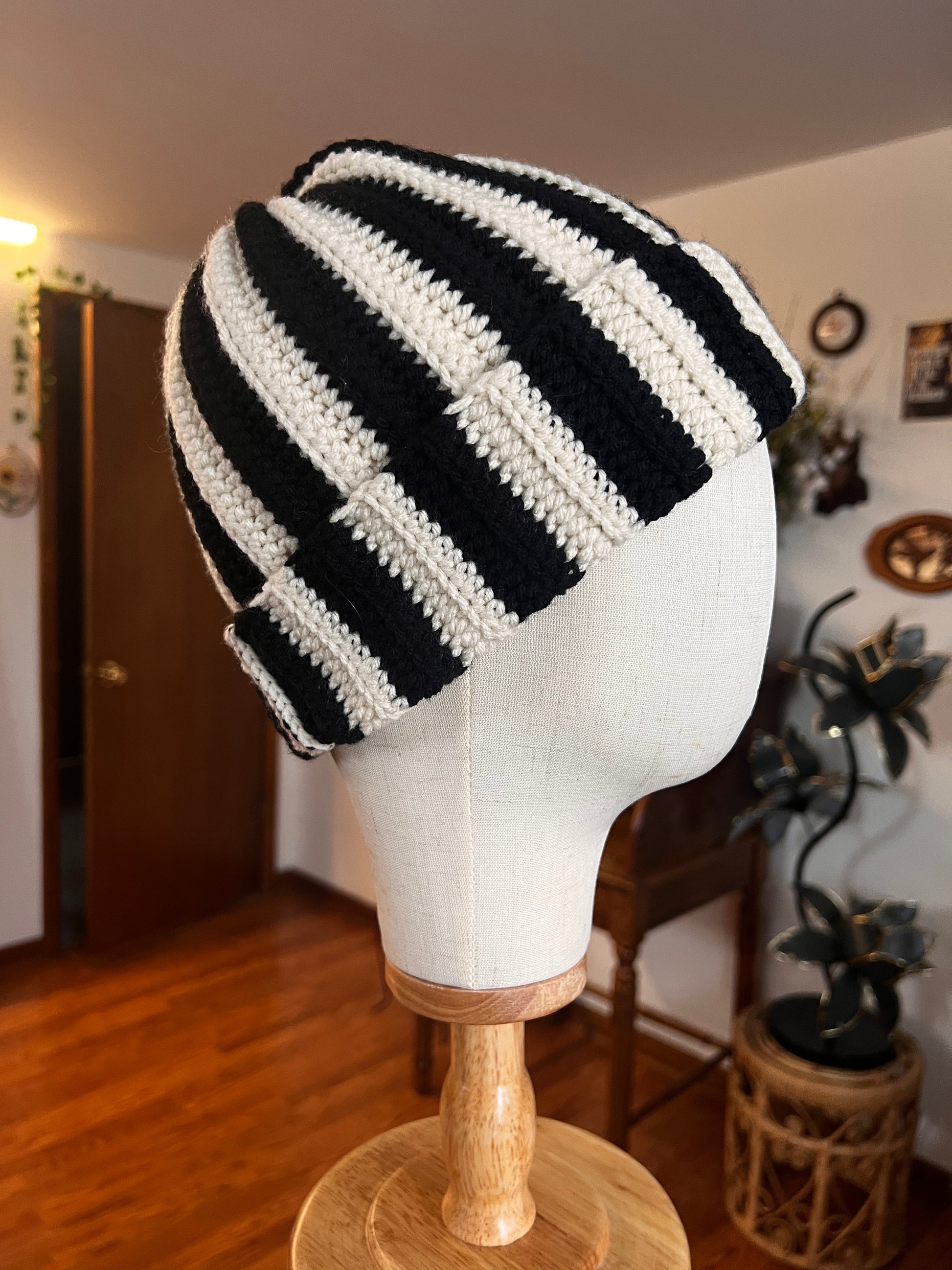 Black and white striped beanie on a mannequin head with a blurred indoor background