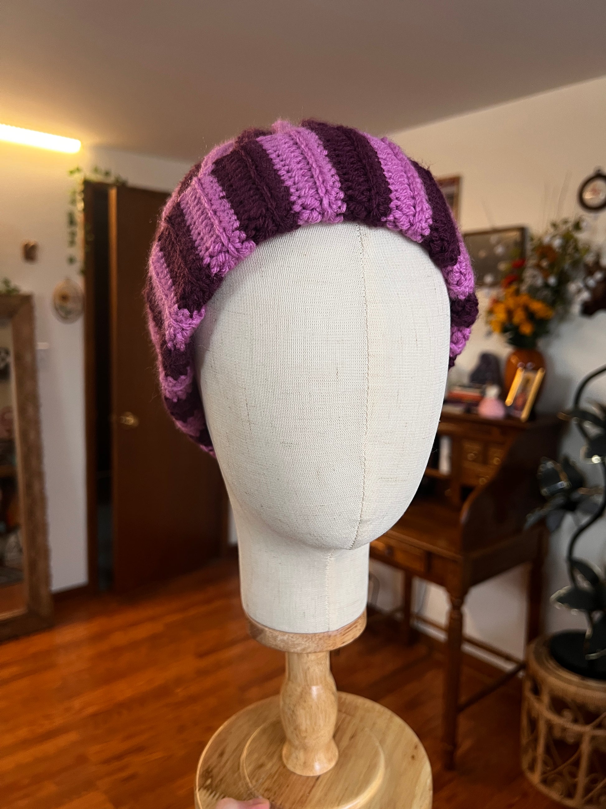 Dark and light purple striped beanie on a mannequin head with a blurred indoor background