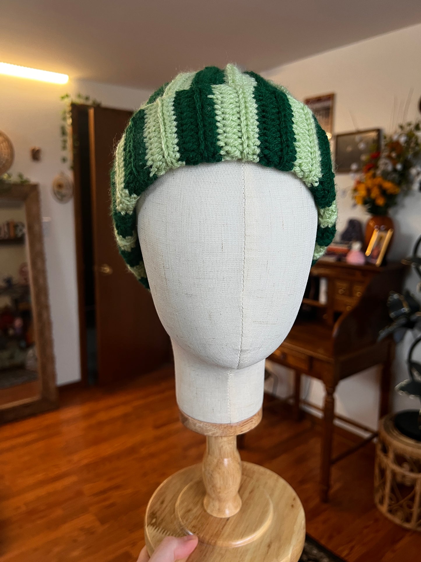 Crochet green striped hat on a mannequin head with a blurred indoor background
