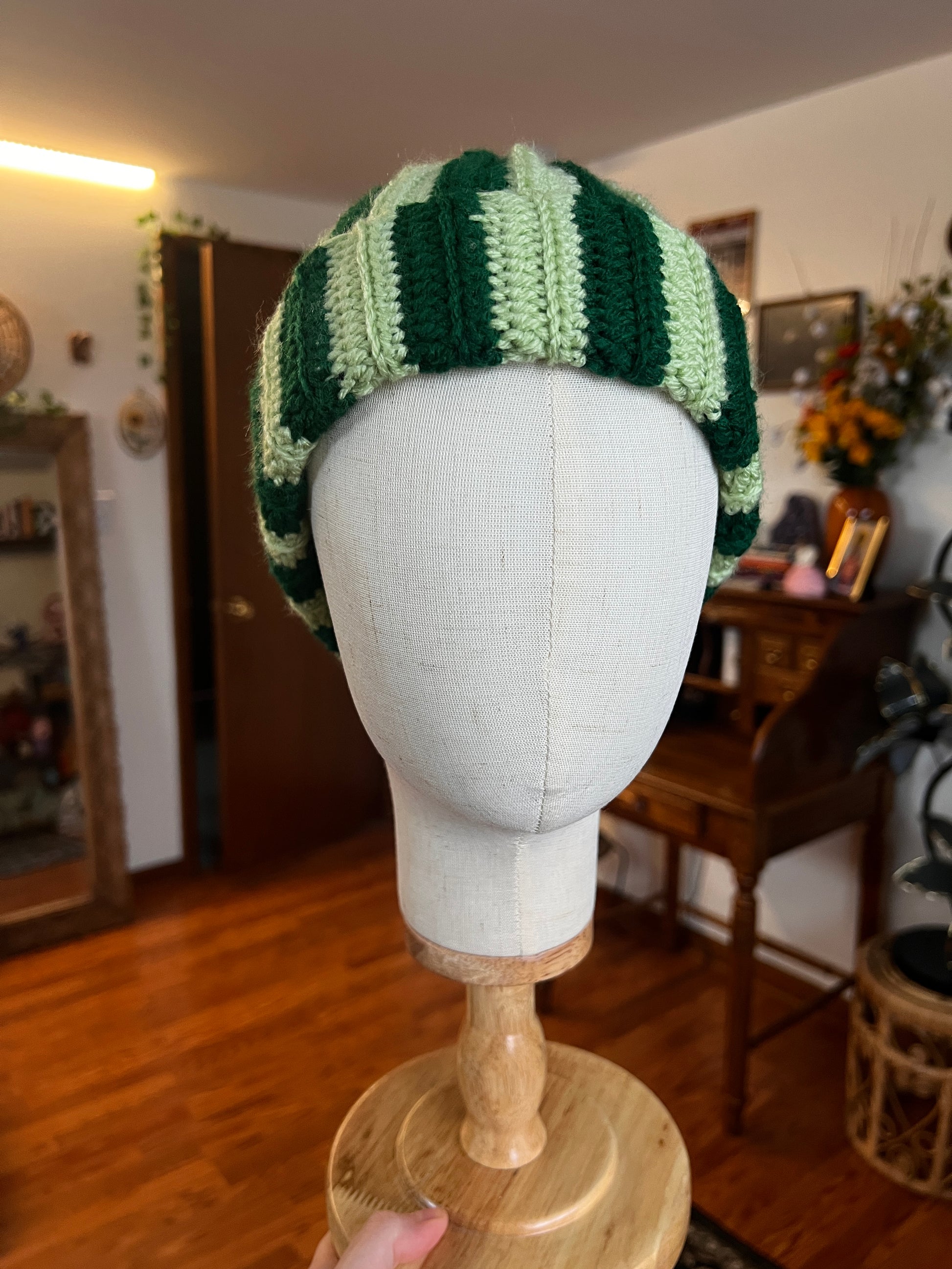 Crochet green striped hat on a mannequin head with a blurred indoor background