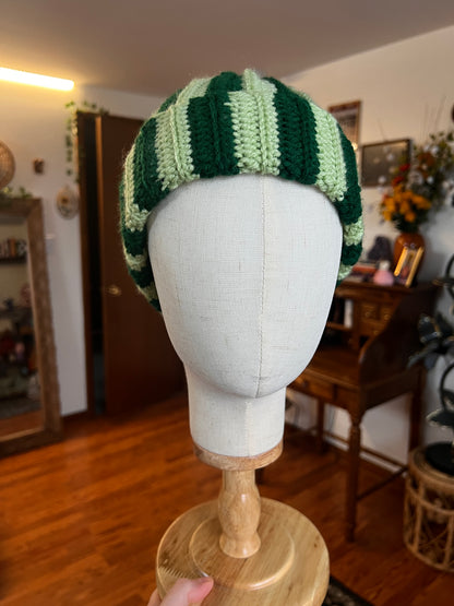 Crochet green striped hat on a mannequin head with a blurred indoor background
