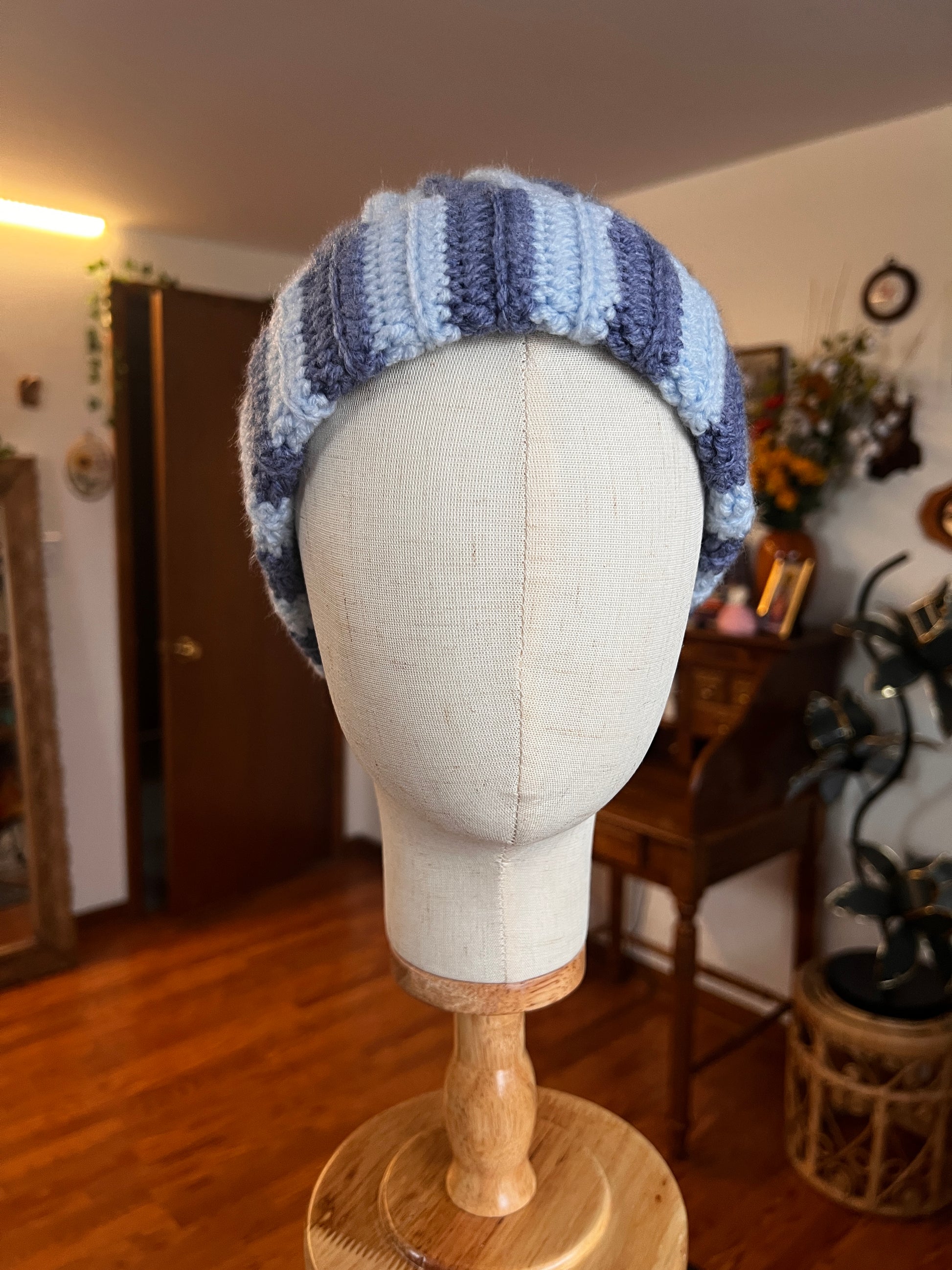 crochet blue beanie on a mannequin head with a wooden base, in a room setting.