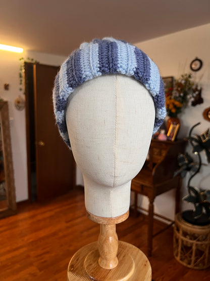 crochet blue beanie on a mannequin head with a wooden base, in a room setting.