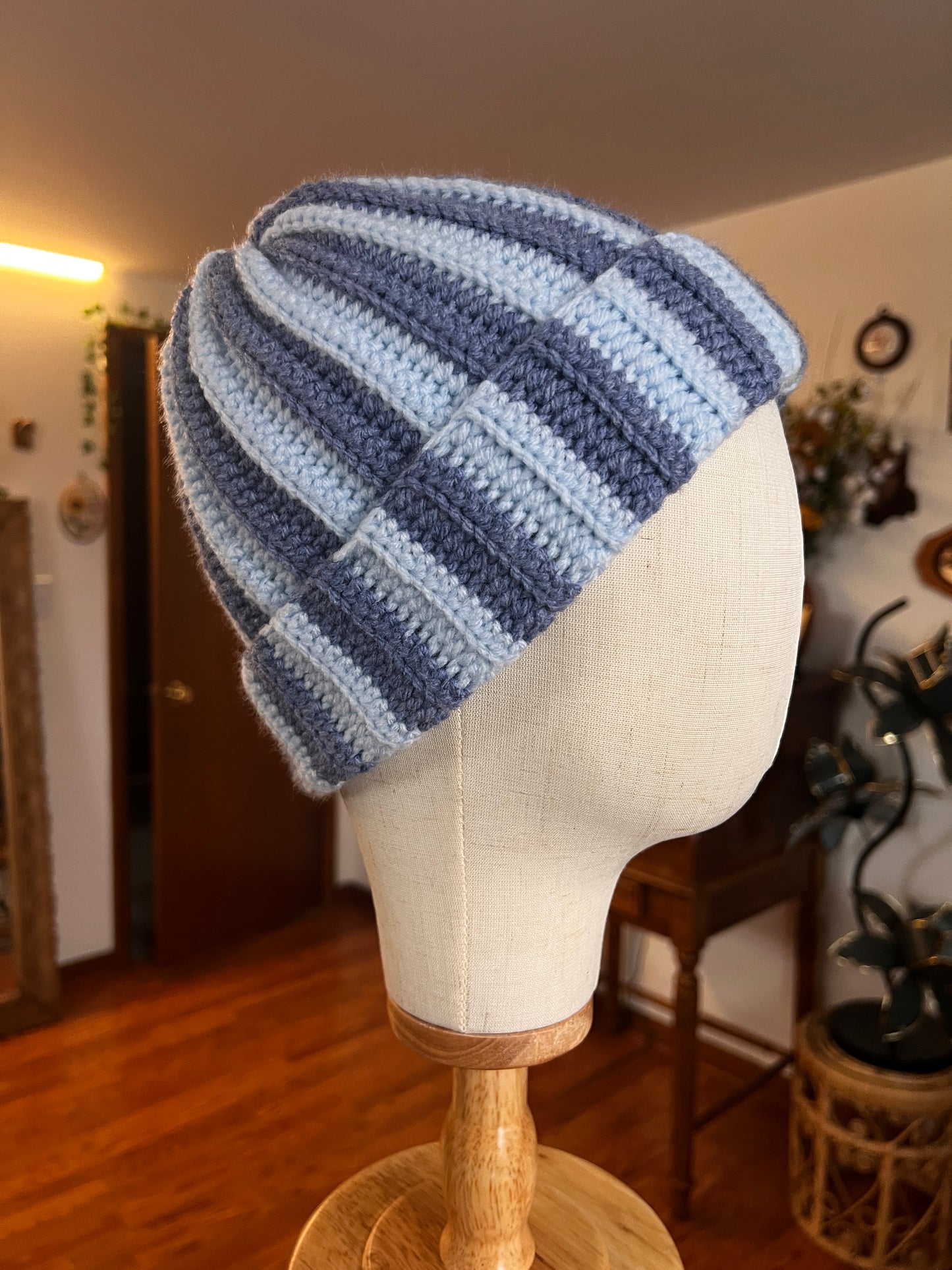 Light and dark blue striped crochet hat on a mannequin head with a blurred indoor background