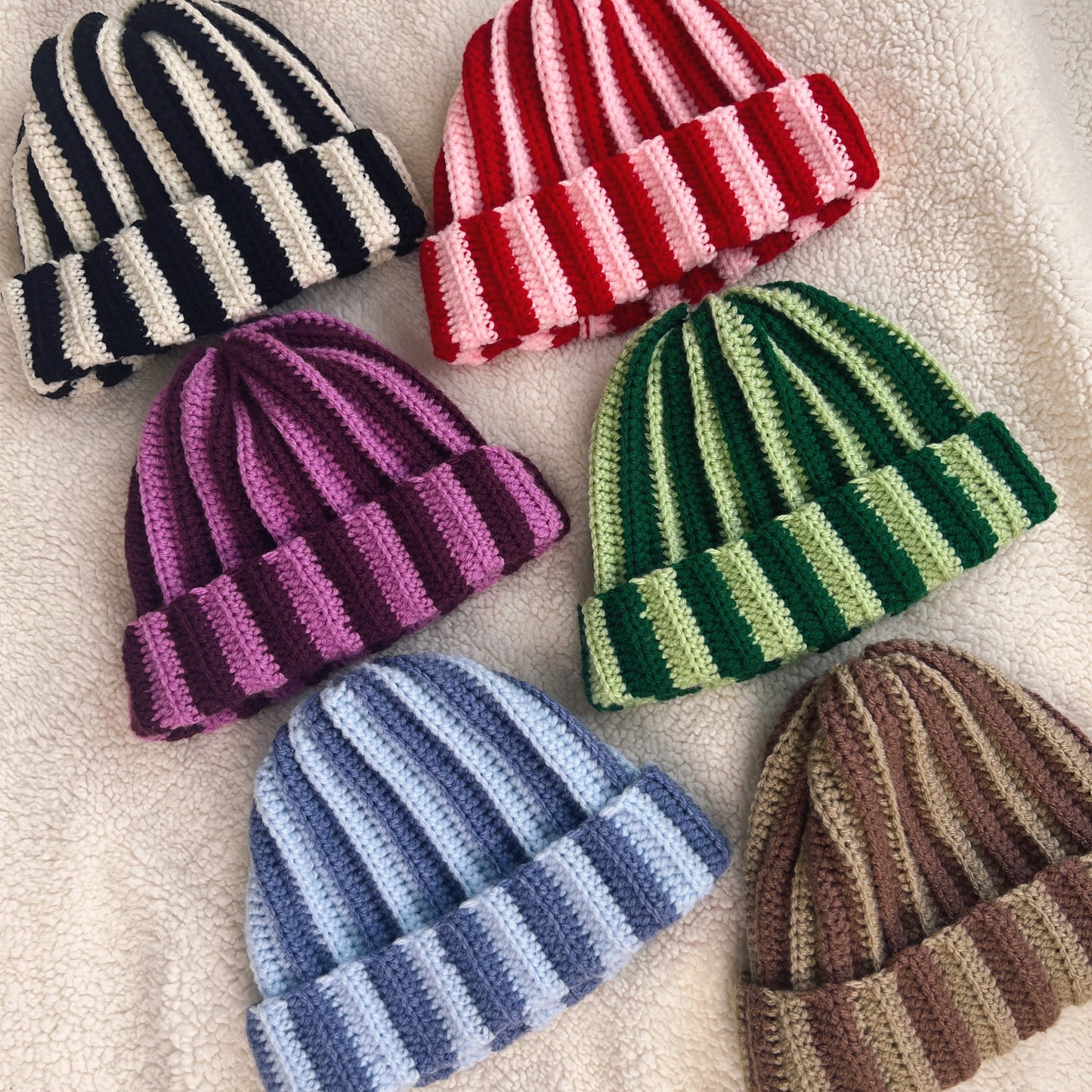 Collection of striped crocheted hats in various colors on a textured surface