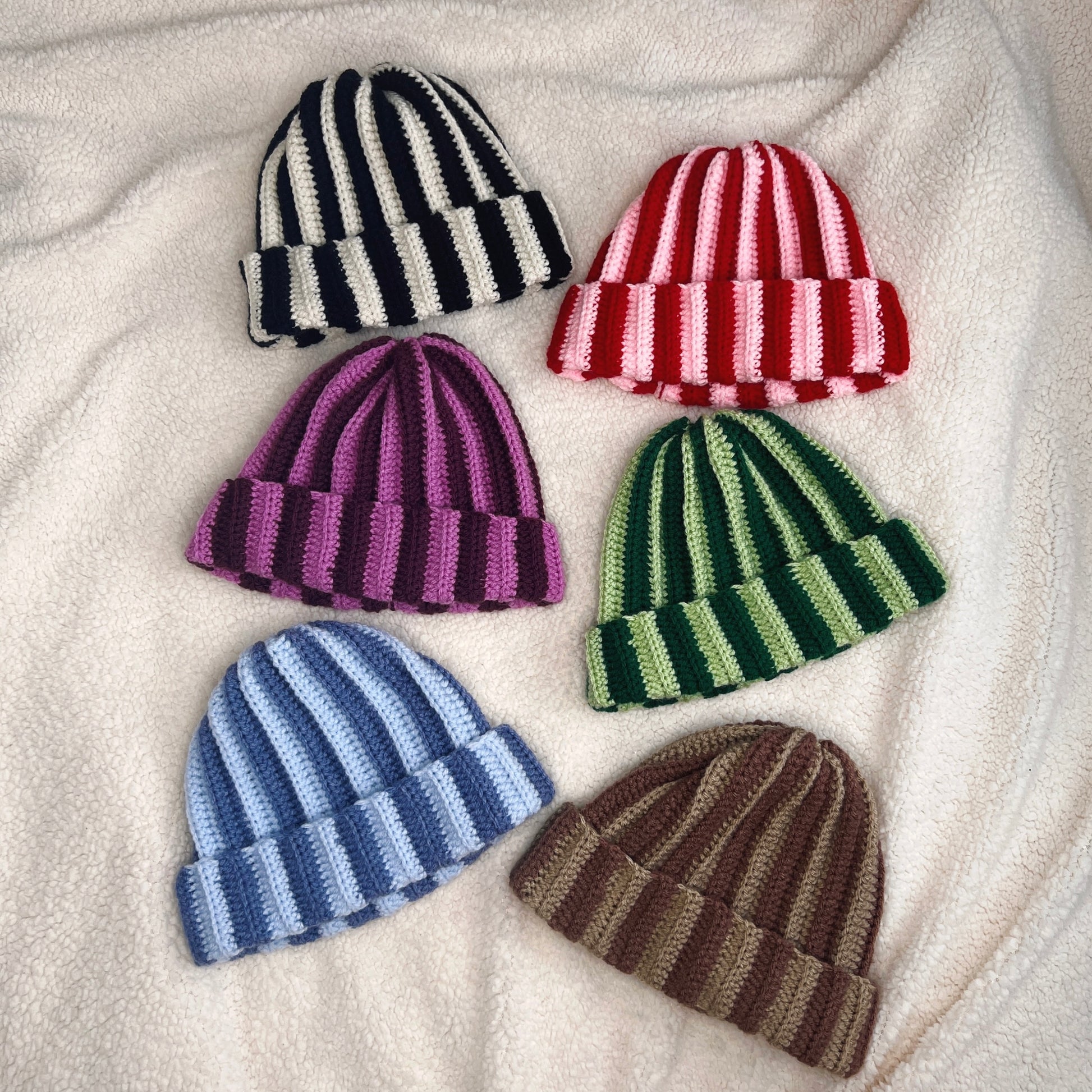 Set of six striped crochet hats in various colors on a soft fabric background