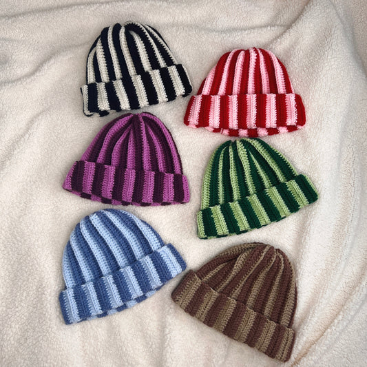 Set of six striped crochet hats in various colors on a soft fabric background
