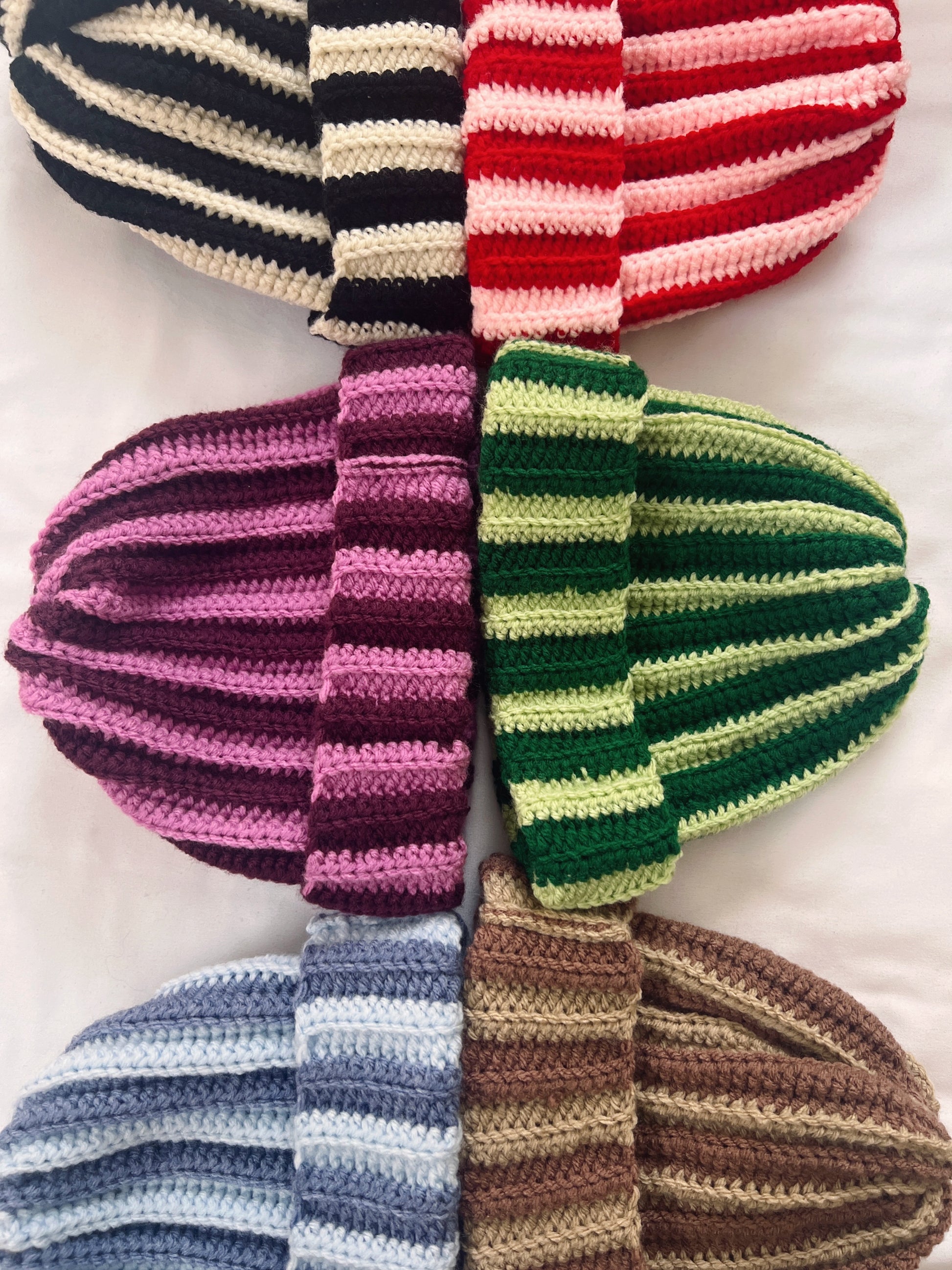 Collection of colorful striped crochet beanie hats on a white background