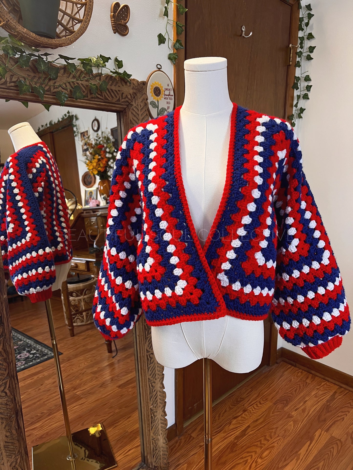 Crochet cardigan in red, white and blue yarn on a mannequin in front of a mirror.