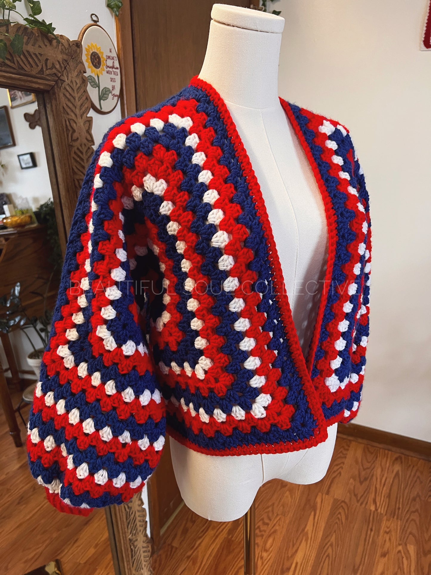 Handmade crochet cardigan in red, white and blue yarn on a mannequin in front of a mirror.
