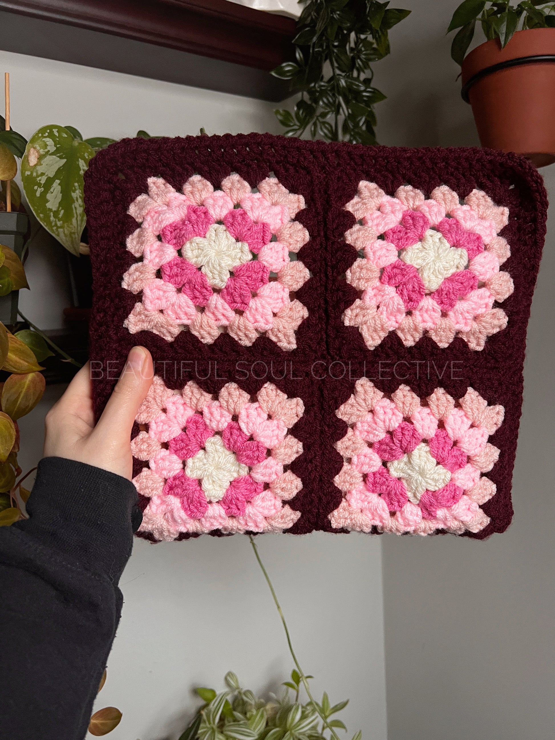 Handmade crochet tablet cover with pink and white square patterns held by a hand.