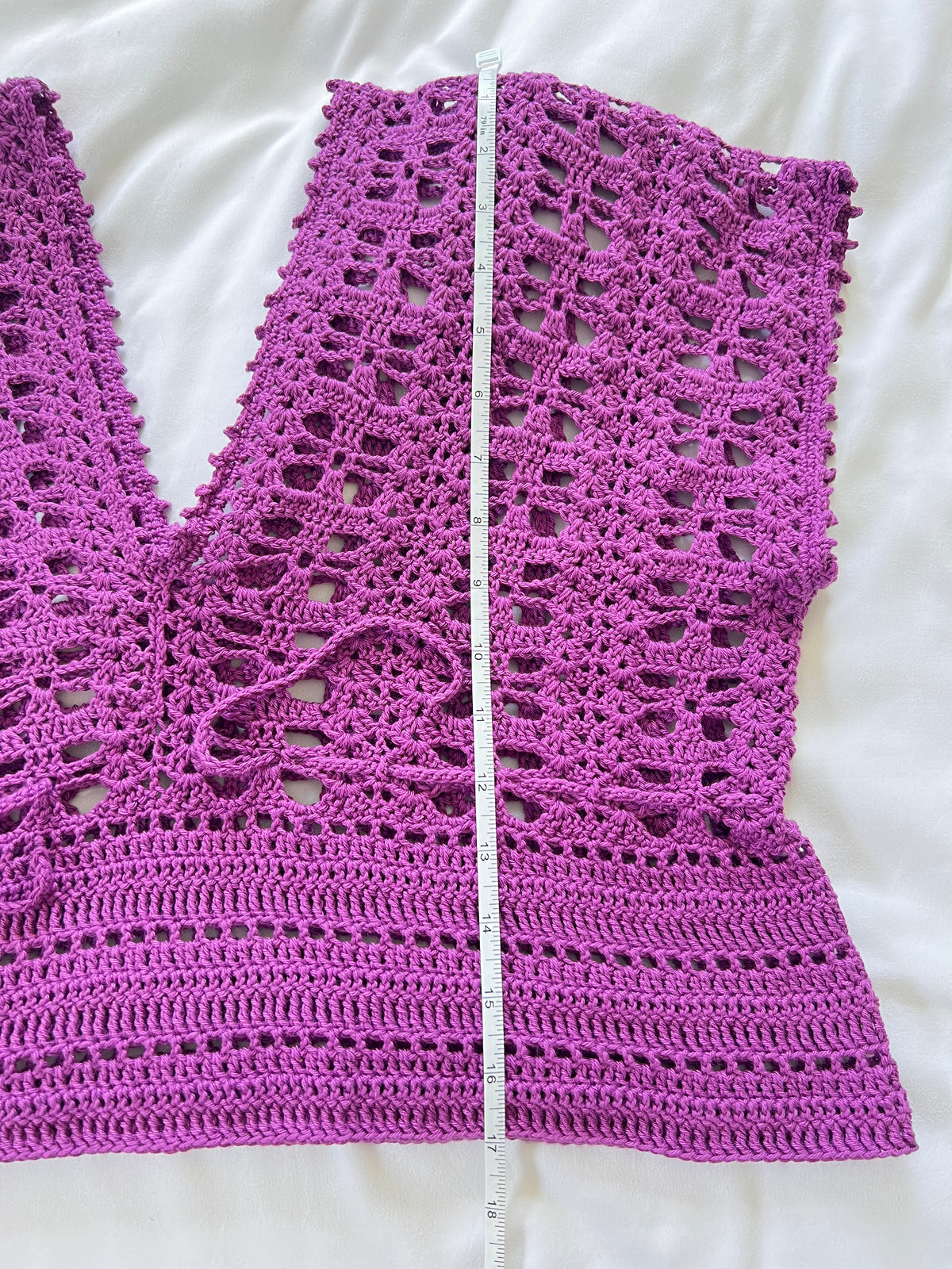 A purple crochet short sleeve top with measuring tape showing the length of garment