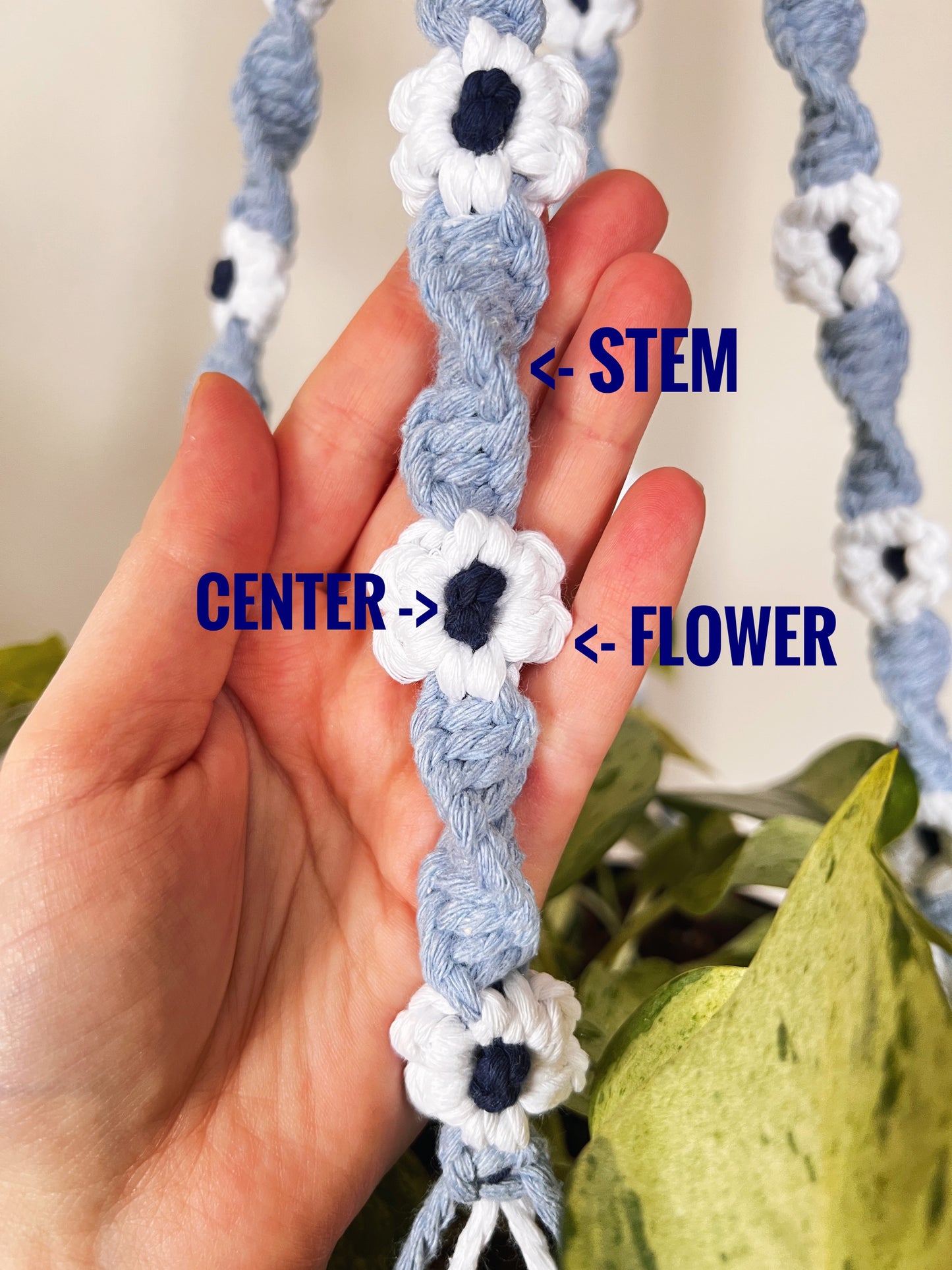 Hand holding a macrame plant hanger with flower designs, labeled 'stem', 'center', and 'flower'.