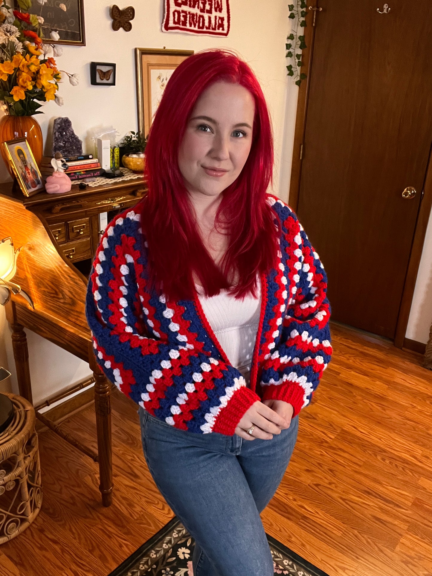 Person wearing a red, white, and blue crochet sweater in a room with wooden floors and furniture.