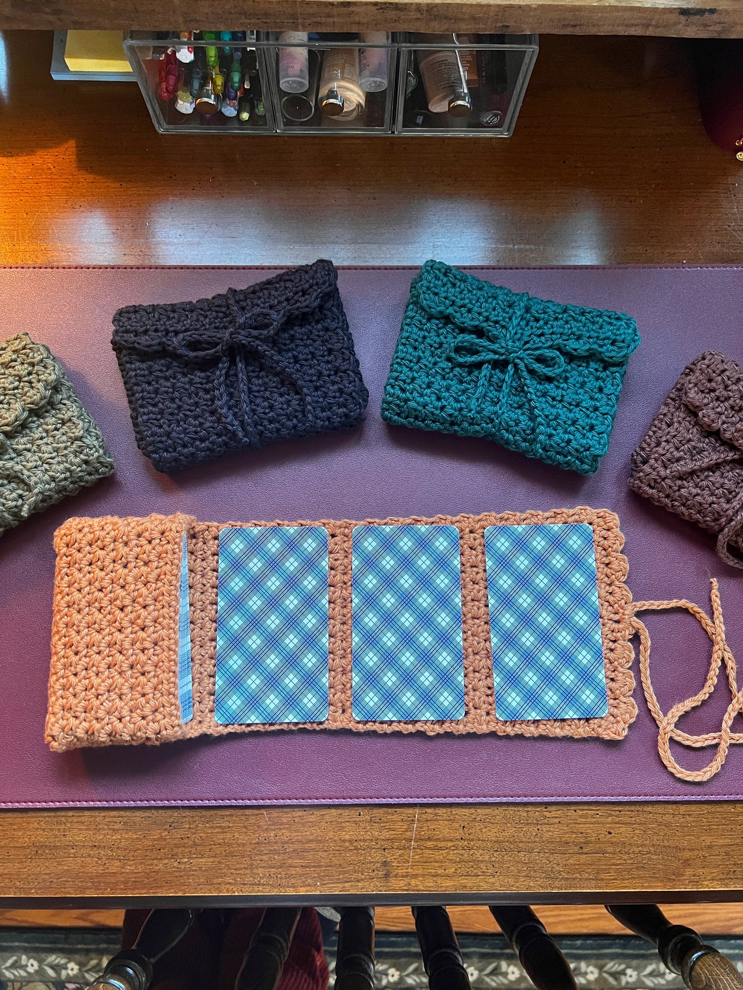 Three crocheted pouches in black, blue, and brown on a purple surface with a checkered pattern.