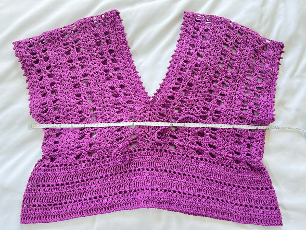 A purple crochet short sleeve top with measuring tape showing the width