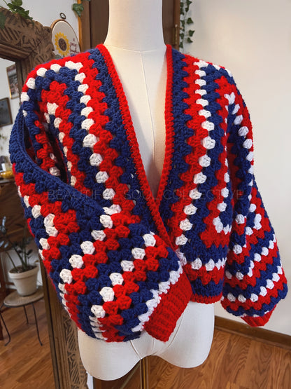 Red, white, and blue handmade crocheted cardigan on a mannequin against a neutral background.